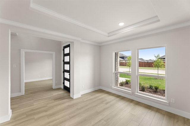 spare room with a tray ceiling, light wood-type flooring, crown molding, and baseboards