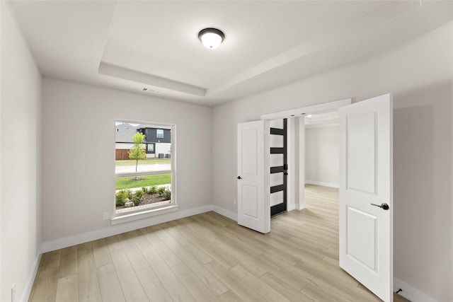 unfurnished bedroom featuring visible vents, baseboards, a tray ceiling, and light wood-style floors
