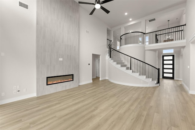 unfurnished living room with visible vents, a high ceiling, ceiling fan, wood finished floors, and stairs