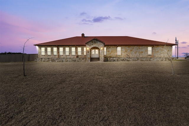 view of front facade featuring a yard, a chimney, stone siding, and metal roof