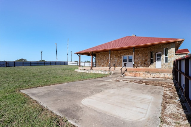 rear view of property featuring fence, a yard, stone siding, and metal roof