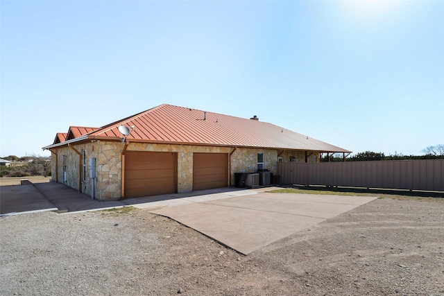 view of front of house featuring central AC unit, fence, concrete driveway, stone siding, and metal roof