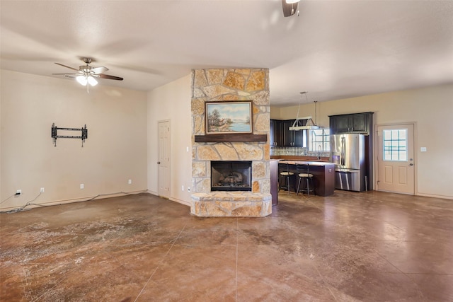 unfurnished living room featuring a stone fireplace, a ceiling fan, and baseboards