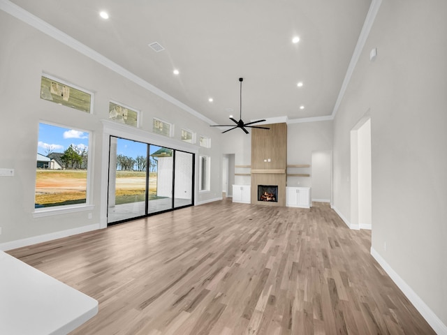 unfurnished living room with a large fireplace, baseboards, ornamental molding, and light wood-style floors