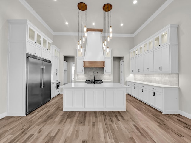 kitchen featuring custom exhaust hood, light countertops, stainless steel built in fridge, white cabinetry, and light wood-type flooring