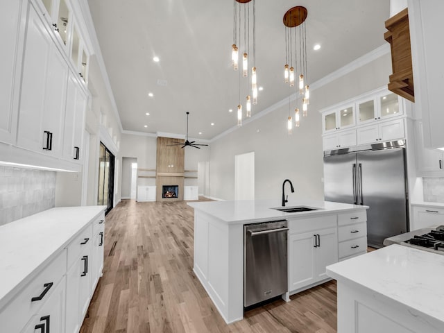 kitchen with a kitchen island with sink, a fireplace, a sink, open floor plan, and appliances with stainless steel finishes