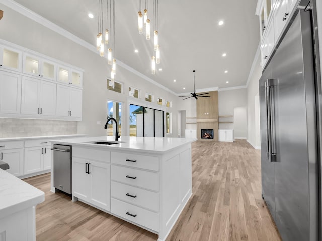 kitchen featuring a sink, light wood-style floors, a lit fireplace, stainless steel built in refrigerator, and crown molding