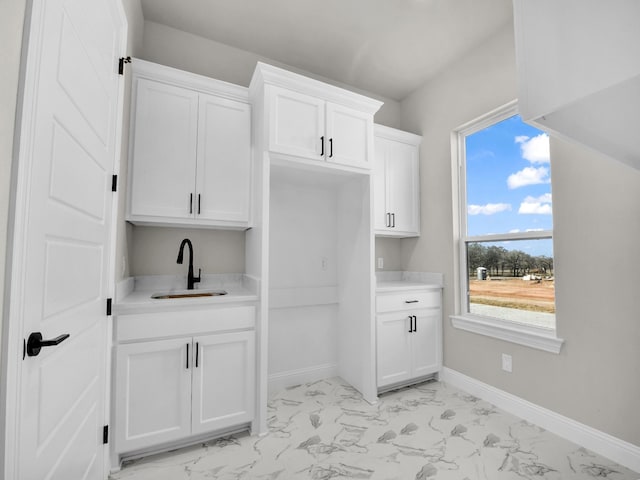 kitchen featuring baseboards, marble finish floor, light countertops, white cabinetry, and a sink