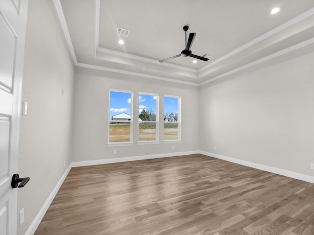 spare room with visible vents, a tray ceiling, wood finished floors, and a ceiling fan