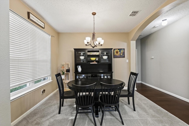 dining area featuring arched walkways, a textured ceiling, baseboards, and a notable chandelier