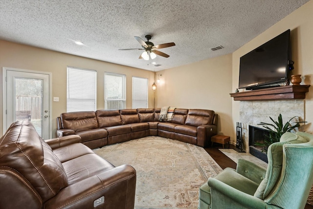 living area with visible vents, a fireplace, a textured ceiling, and ceiling fan