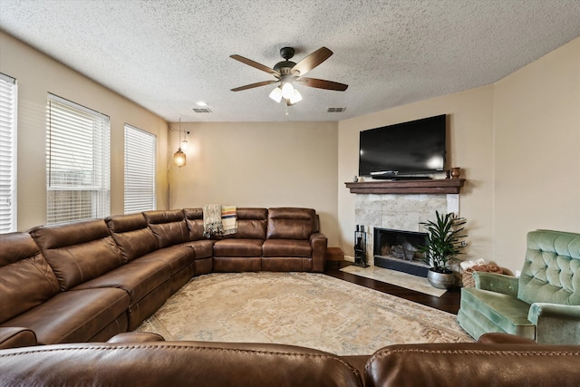 living area with visible vents, a tiled fireplace, a ceiling fan, wood finished floors, and a textured ceiling