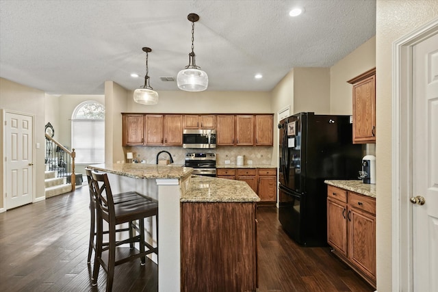 kitchen with visible vents, brown cabinetry, decorative backsplash, appliances with stainless steel finishes, and dark wood-type flooring