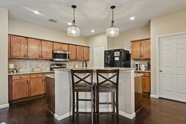 kitchen with a kitchen island with sink, stainless steel appliances, dark wood-type flooring, visible vents, and brown cabinetry