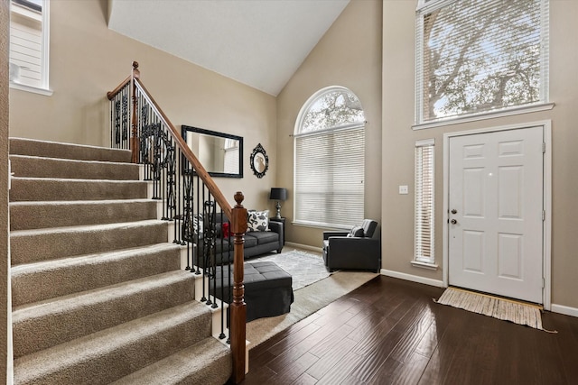 foyer with high vaulted ceiling, stairway, wood finished floors, and baseboards