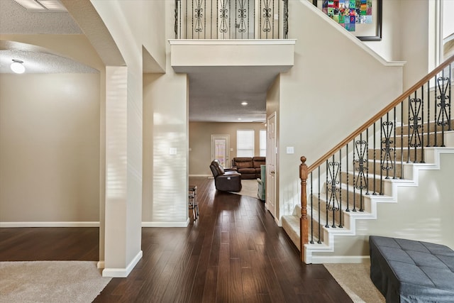 foyer entrance with baseboards, arched walkways, a towering ceiling, wood-type flooring, and stairs