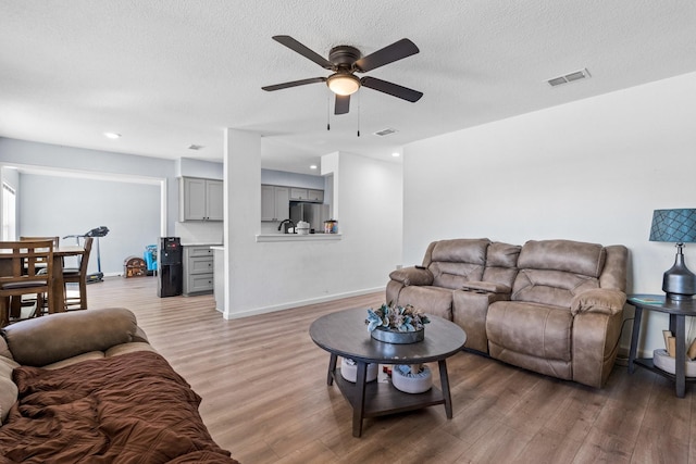 living area featuring light wood finished floors, visible vents, and a textured ceiling