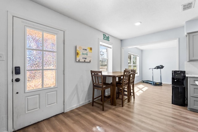 dining room featuring light wood-style flooring, a textured ceiling, visible vents, and baseboards