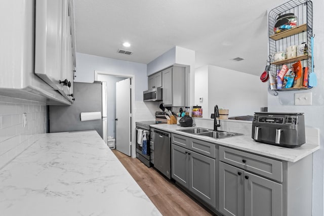 kitchen with visible vents, stainless steel appliances, gray cabinetry, light wood-style floors, and a sink