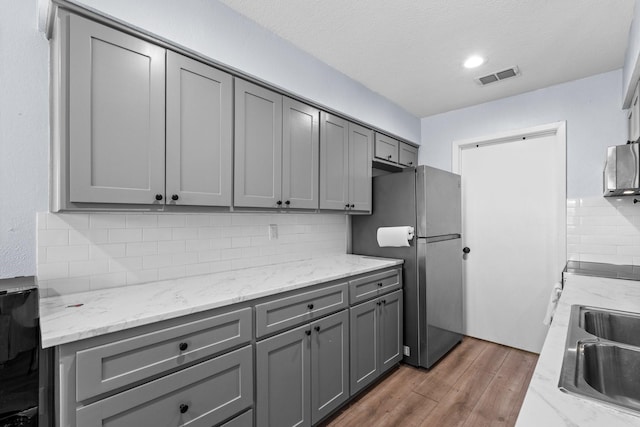 kitchen featuring gray cabinetry, a sink, visible vents, backsplash, and freestanding refrigerator