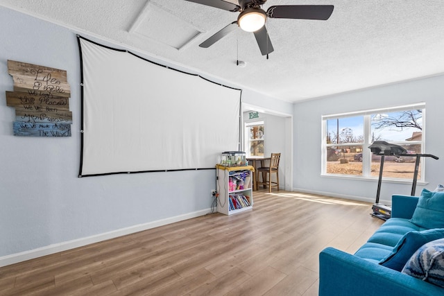 living area featuring a textured ceiling, ceiling fan, wood finished floors, and baseboards