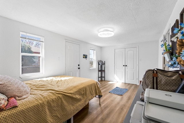 bedroom with a textured ceiling, multiple windows, a closet, and light wood-style floors