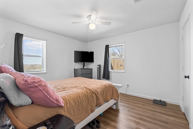 bedroom with a textured ceiling, multiple windows, wood finished floors, and baseboards