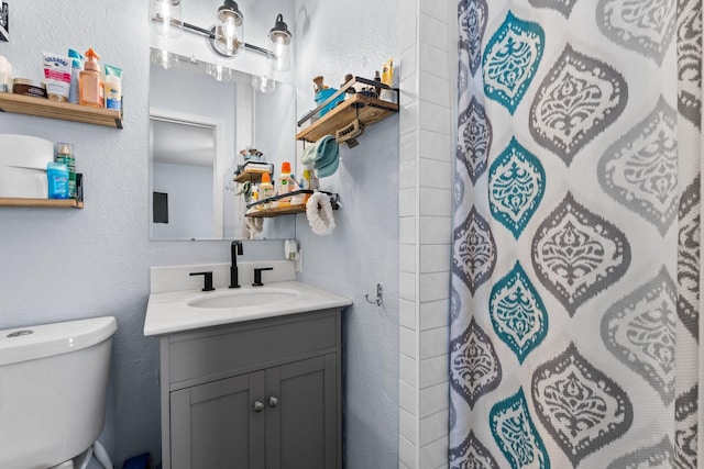 bathroom with toilet, a textured wall, a shower with shower curtain, and vanity