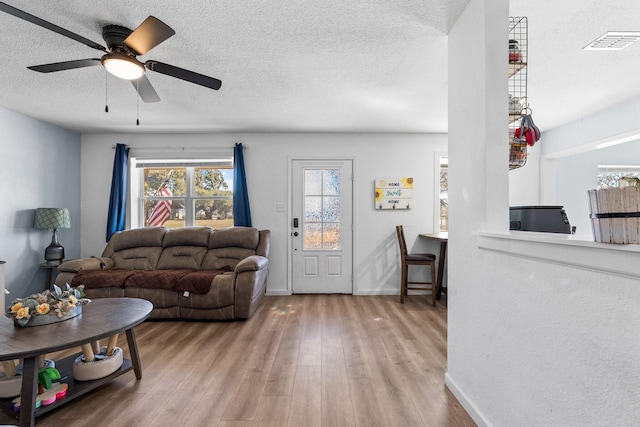 living area featuring visible vents, a textured ceiling, baseboards, and wood finished floors