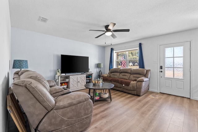 living area featuring light wood-style floors, visible vents, a textured ceiling, and a ceiling fan