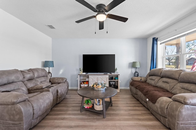 living room with a textured ceiling, baseboards, visible vents, and light wood-style floors