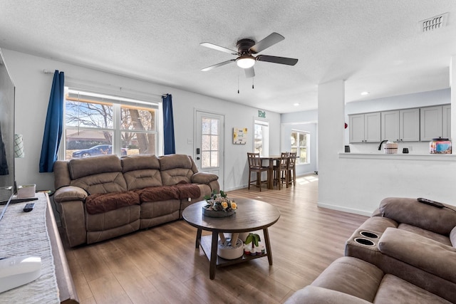 living area with light wood-type flooring, visible vents, a textured ceiling, and baseboards