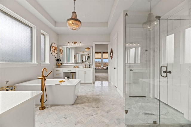 bathroom featuring vanity, a tray ceiling, a soaking tub, and a shower stall