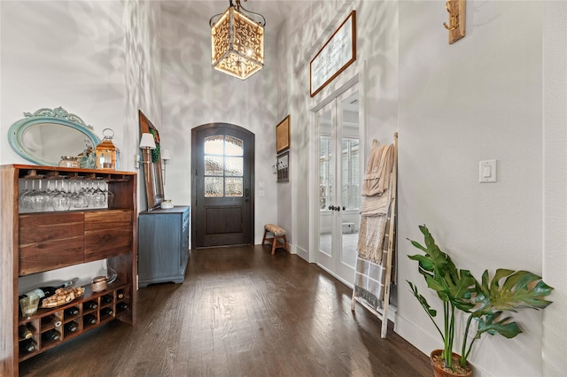 entryway featuring baseboards, arched walkways, french doors, a towering ceiling, and dark wood-style floors