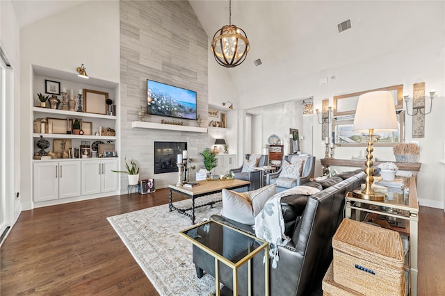 living room featuring built in features, wood finished floors, visible vents, a tile fireplace, and a notable chandelier