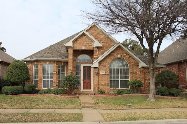 traditional home with brick siding, a shingled roof, and a front lawn