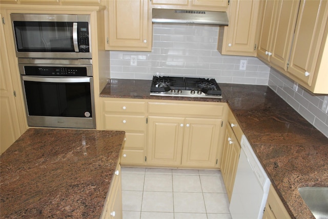 8509 Mustang Dr, Irving, TX 75063 - kitchen with light tile patterned floors, dark stone counters, under cabinet range hood, appliances with stainless steel finishes, and backsplash