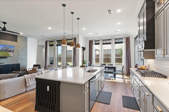 kitchen featuring a center island with sink, stainless steel appliances, light countertops, light wood-type flooring, and a sink