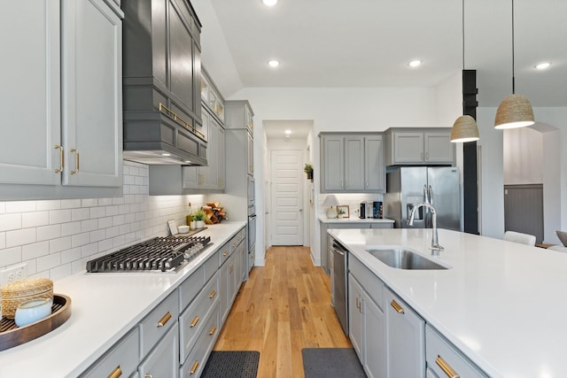 kitchen featuring appliances with stainless steel finishes, a sink, gray cabinetry, light countertops, and light wood-style floors