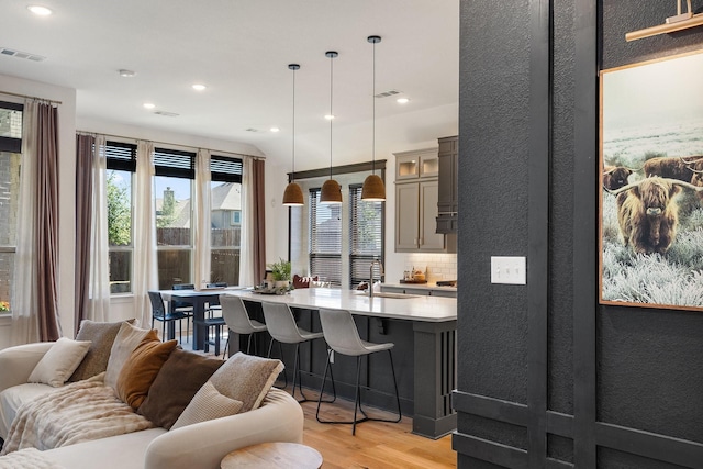 kitchen featuring light countertops, visible vents, glass insert cabinets, light wood-type flooring, and a kitchen breakfast bar