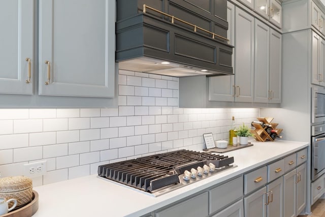 kitchen with tasteful backsplash, stainless steel appliances, gray cabinets, light countertops, and custom range hood