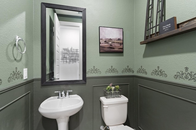 half bathroom with a wainscoted wall, a sink, toilet, and a decorative wall