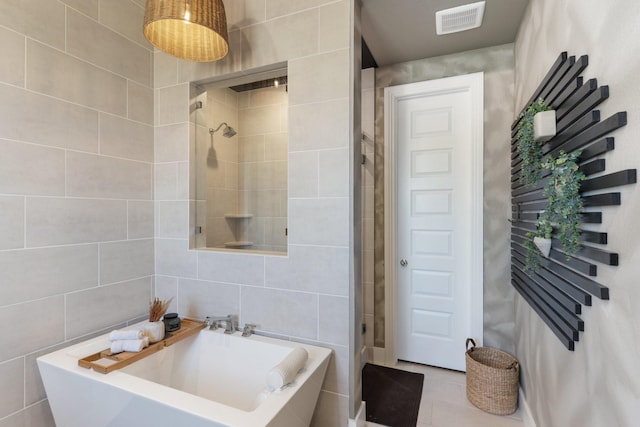 bathroom with a tile shower, tile patterned floors, a washtub, tile walls, and visible vents