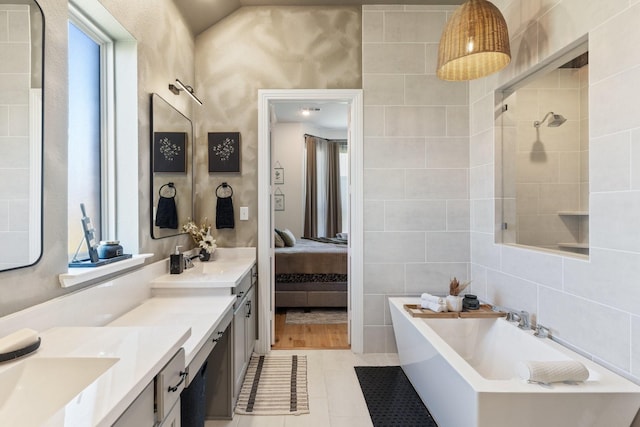 full bathroom with a sink, double vanity, a freestanding tub, and tile walls