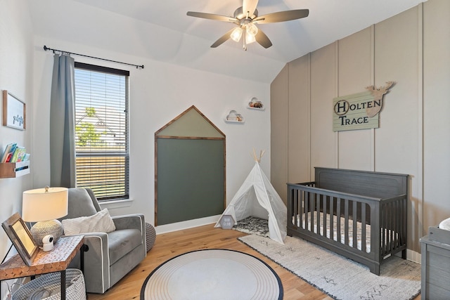 bedroom with lofted ceiling, baseboards, a nursery area, a ceiling fan, and light wood-style flooring