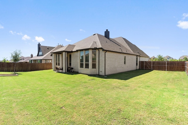 rear view of house featuring brick siding, a fenced backyard, a chimney, and a yard