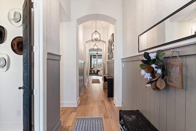 hall featuring arched walkways, light wood finished floors, and baseboards