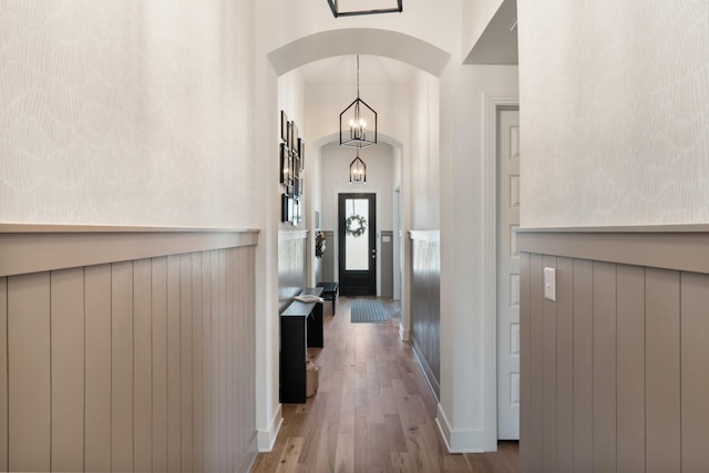 corridor with baseboards, arched walkways, a chandelier, and wood finished floors