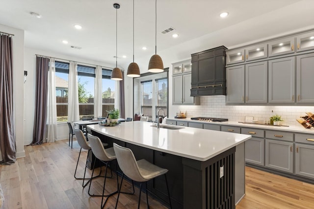 kitchen featuring a sink, stainless steel gas stovetop, backsplash, visible vents, and a center island with sink