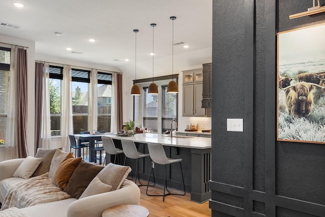 kitchen featuring visible vents, light wood-style floors, a kitchen bar, light countertops, and a sink